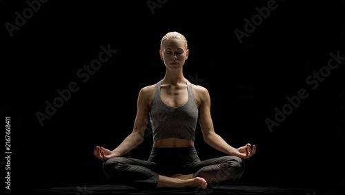 Young woman practicing yoga meditation sitting in lotus position on dark background with meditation wellness exercise mindfulness lifestyle serenity