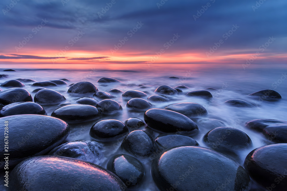 Fototapeta premium Round black stones on a calm sea shore at twilight