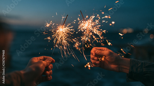 Hands hold sparklers together at dusk by the ocean