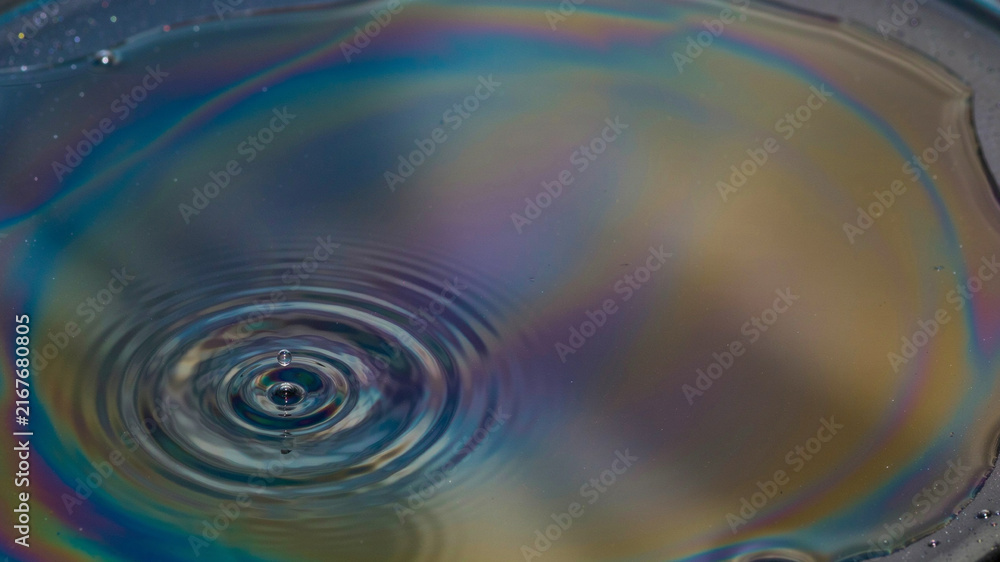 Fototapeta premium Iridescent Swirls: A close-up view of an iridescent oil slick on water, creating a mesmerizing pattern of rainbow colors with concentric ripples from a water drop.