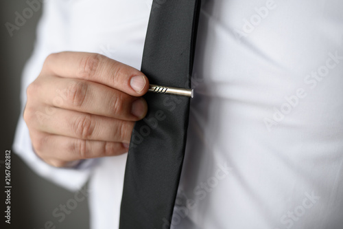 Fotografía Man adjusting silver tie clip on black necktie close up, elegant groom wedding a