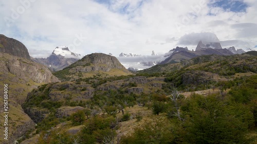 Panoramic view of Patagonia wilderness: rocky mountains, green forests, and snow-capped peaks of El Chaltén under a cloudy sky