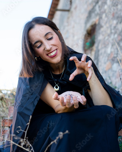Woman with Spider on Palm Conjuring Magic in Front of Stone Wall