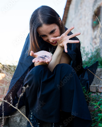 Woman in Black Cloak Holding Spider on Stone Steps