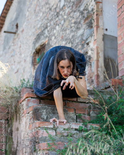 Woman in Cape Crouching and Reaching on Rustic Brick Wall