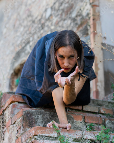 Woman in Cape Crouching and Reaching on Rustic Brick Wall