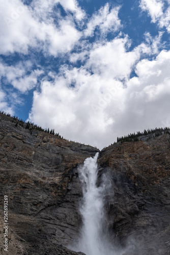 Takakkaw Falls in Yoho National Park, Canada, cascading down a dramatic Rocky Mountain cliff above dense evergreen forest on a scenic summer day.