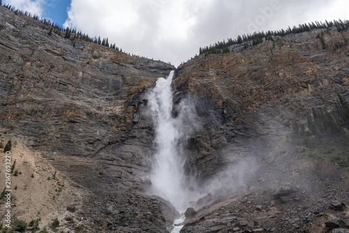 Takakkaw Falls in Yoho National Park, Canada, cascading down a dramatic Rocky Mountain cliff above dense evergreen forest on a scenic summer day.