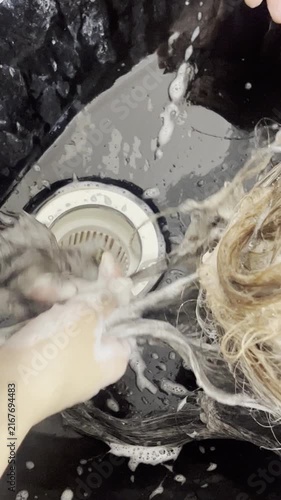 Hairdresser hands washing woman hair in black sink close up 9:16 vertical, beauty salon concept