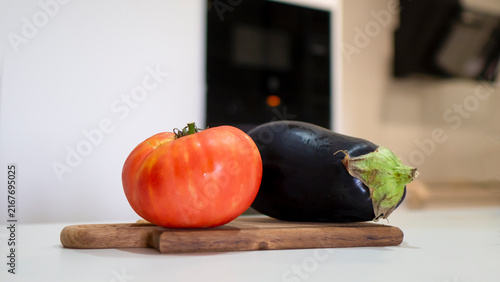 A large, ripe tomato and an eggplant on a wooden cutting board.