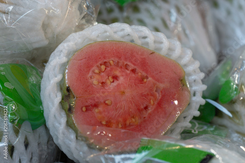 Quadro su tela Macro view of a juicy ripe pink guava cut in half, encased in white protective foam net packaging at an Asian grocery market