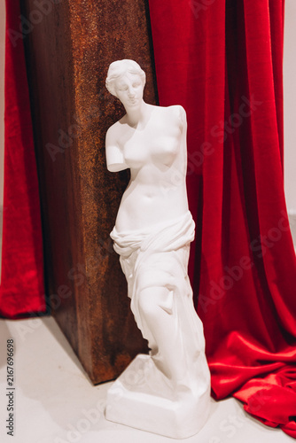 Foto Venus de Milo Replica: An elegant white plaster replica of the Venus de Milo stands tall, draped in rich red satin fabric, evoking classical artistry and timeless beauty