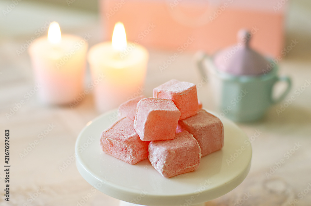 Fototapeta premium Cubes of rose Turkish delight candy in a pastel setting with candles 