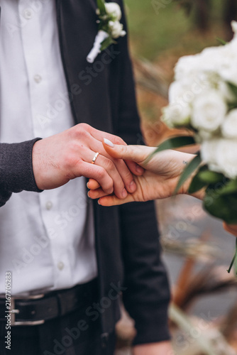 Foto A Sacred Vow: Close-up shot of a couple exchanging wedding rings, symbolizing their eternal love and commitment on their special day, with a white bouquet in the foreground
