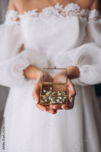 Bild auf Leinwand Bridal Treasures: A bride in a delicate white gown gently holds a small, ornate glass box filled with tiny white flowers, showcasing a moment of anticipation and cherished sentiment