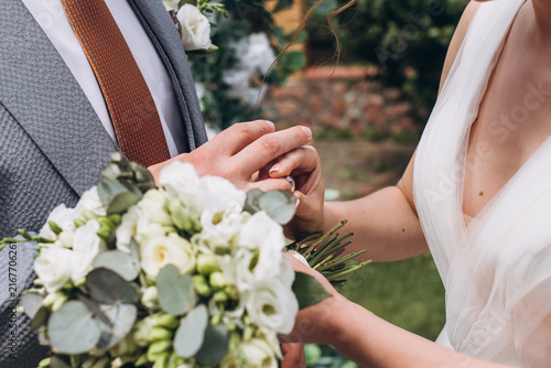 Canvas Print Exchange of Vows: A tender moment captured as a bride and groom exchange wedding rings during their outdoor ceremony, surrounded by nature's beauty, symbolizing eternal love and commitment