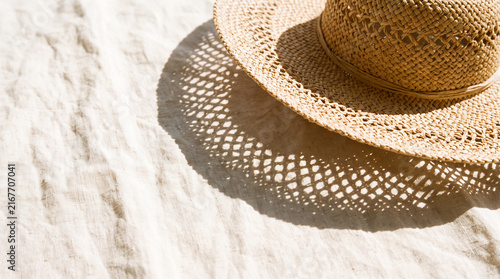 Straw hat casting patterned geometric shadow on crumpled beige linen fabric with harsh bright sunlight and copy space