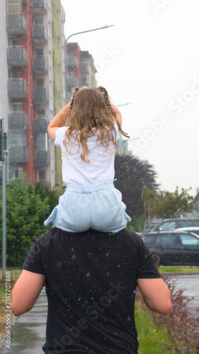 Father Carrying Daughter On Shoulders Running Through Heavy Summer Rainstorm On City Street