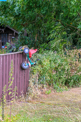 Obraz na płótnie Bright kids tricycle bicycle hanging on brown wooden fence in rural garden