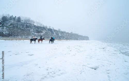 Konstfotografi A group of riders rides along the shore of a frozen lake during a snowfall