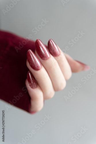 Glossy Dark Red Cat Eye Manicure, Magnetic Velvet Gel Nails, Professional Nail Art – Curved female fingers featuring long almond-shaped burgundy fingernails with a metallic shimmering effect