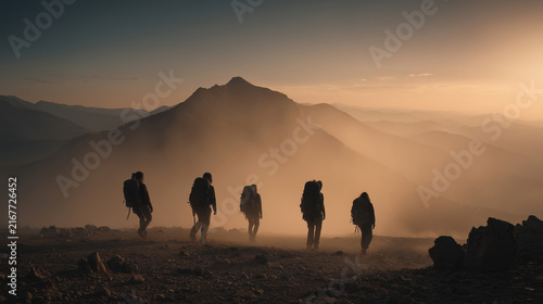 Group of hikers trekking through misty mountain valley at sunrise, silhouetted against golden light with dramatic peaks in background during outdoor adventure expedition.