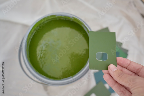 Hand holds green paint sample beside open can of similar green paint