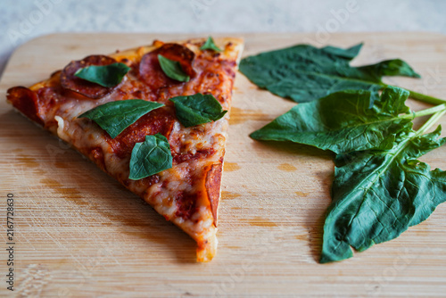 Pepperoni pizza slice next to fresh spinach leaves