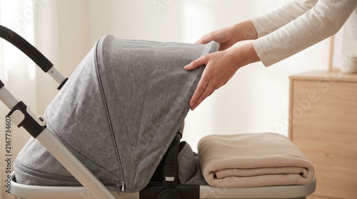 Hands adjusting the grey fabric canopy of a modern baby stroller near a blanket