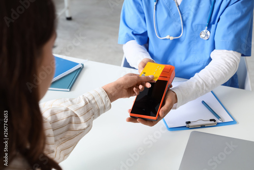 Female patient with credit card and doctor paying via terminal at table in cl...