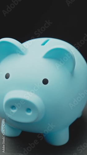 Close-up of cute blue piggy bank rotating at black background. Save money for your dream. Finance and investment concept. Vertical video. Close-up in 4K, UHD