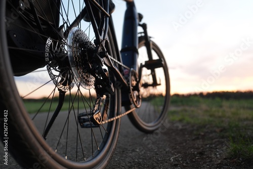 Electric bicycle rear wheel close-up with cassette, derailleur, chain and disc brake on an outdoor path at sunset, with blurred background and ample copy space on the right