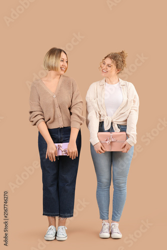 Beautiful happy women in stylish jeans with gift boxes on beige background