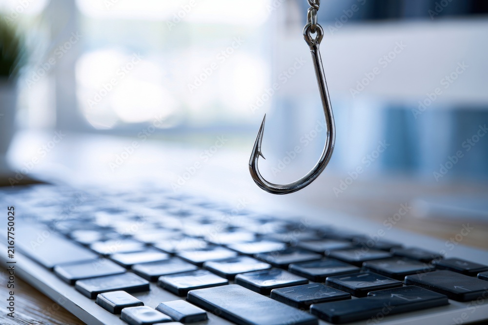 Naklejka premium Concept of cybercrime and online fraud with a metal fishhook hovering above a computer keyboard symbolizing digital phishing attacks and scams
