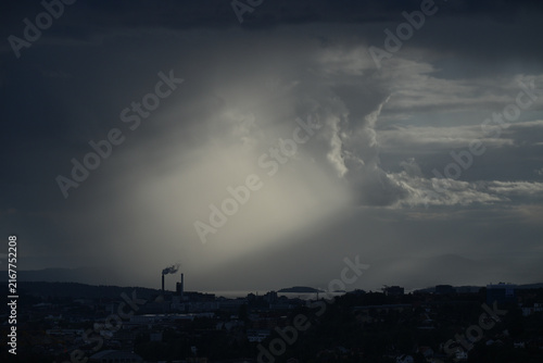 Canvas Print Dramatic Light Beam Breaking Through Dark Storm Clouds Over Coastal City Skyline