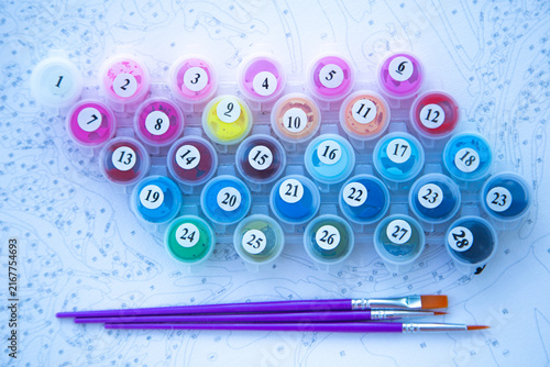 Top view of a set of paints with jars from 1 to 28 and three brushes on canvas. Concept of creativity, painting by numbers, hobbies, art therapy. High quality photo