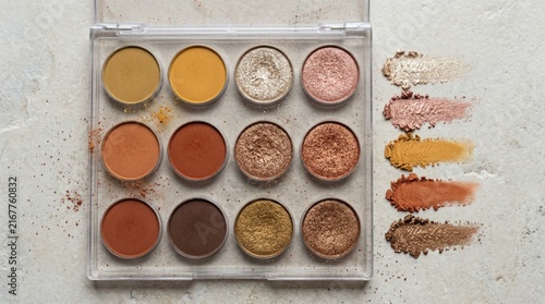 Overhead flat lay of eyeshadow palette with matte ochre and terracotta shades beside shimmering champagne bronze pans and powder swatches on stone background