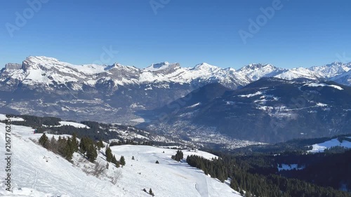 Wide panoramic view of the French Alps above Passy and Chamonix, showing snow-covered mountains, forested slopes, and a clear blue sky.
