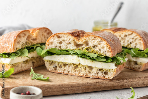 Fresh ciabatta sandwich with mozzarella, arugula and pesto sauce close up, toasted italian panini, rustic deli