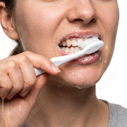 A woman brushing her teeth vigorously with a toothbrush, foam and water dripping from her mouth. Her expression shows concentration and perhaps a slight grimace