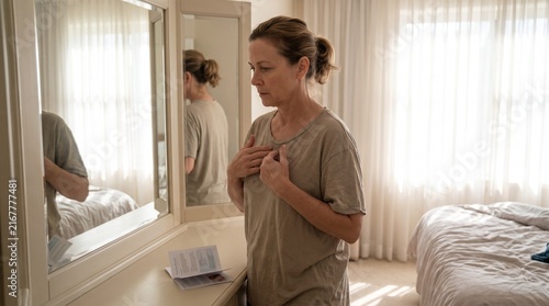 Woman looking in mirror with hands on chest in bedroom with soft light