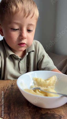A cute little boy eating delicious handmade dumplings from a white bowl while sitting at a wooden table.