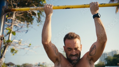Fotografie Man doing intense pull-ups on a bar at an outdoor gym, building strength and mus