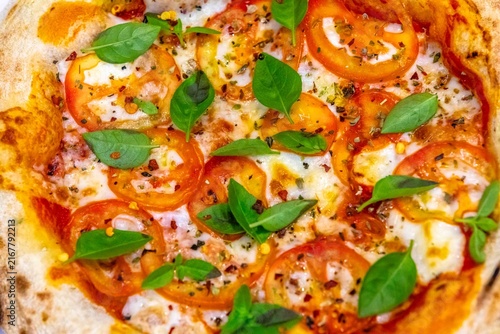 Neapolitan-style personal pizza with naturally leavened long-fermentation dough, sliced tomatoes, melted mozzarella, fresh basil and oregano, served on a white plate over a dark pinstriped cloth.