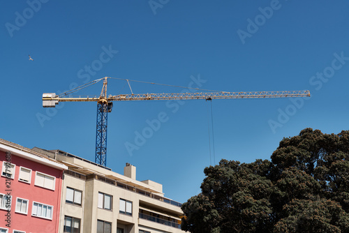 Картината върху платно Yellow tower crane extending boom above residential apartment buildings and tree