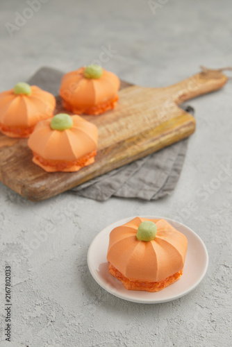 Single pumpkin shaped dessert on a small plate with others in the background on a wooden board