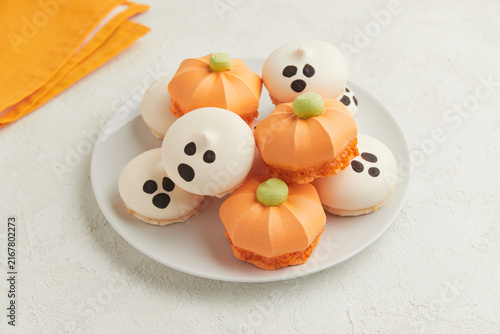 Orange pumpkin shaped meringue desserts and ghost shaped meringue cookies on a white plate