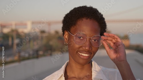 Portrait of a smiling Black African American woman wearing eyeglasses on a waterfront promenade at sunset.
