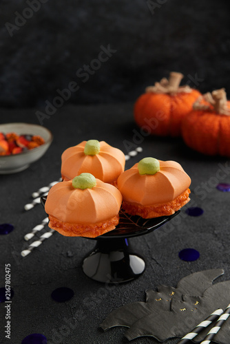 Pumpkin shaped desserts with green tops on a black stand, set against a dark background