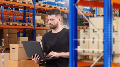 Konstfotografi Warehouse inventory management, worker uses laptop to check stock records and coordinate storage of boxes and goods on pallet racks